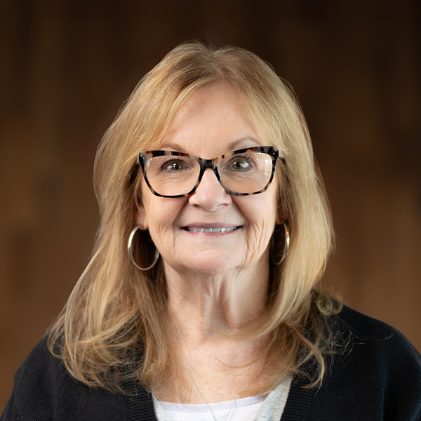 Deidre Rombach, Resident Services Director at The Boulevard of Wentzville, wearing tortoiseshell glasses and a black cardigan, smiling warmly against a softly lit background.