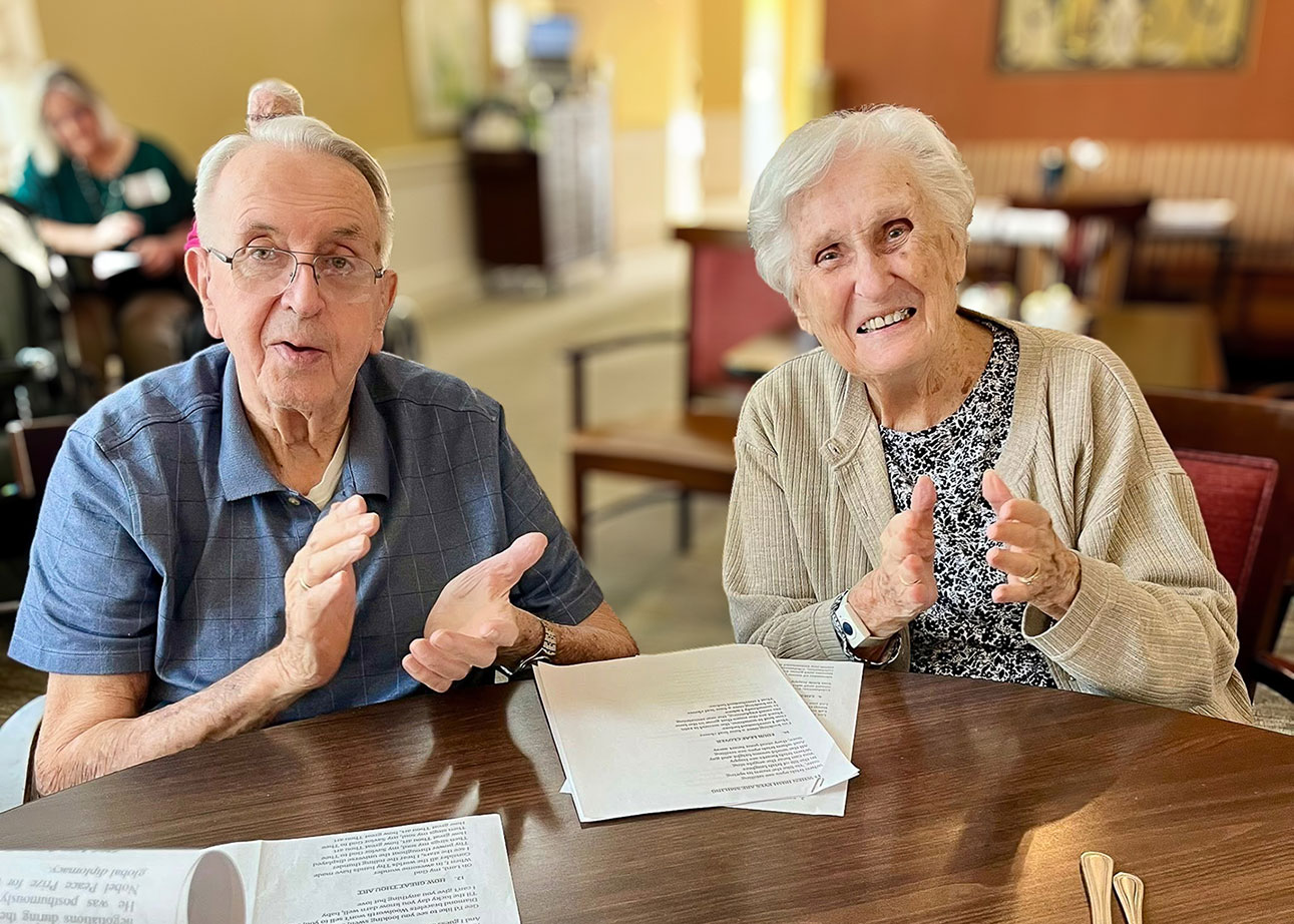Two seniors smile and clap, taking part in a fun event.