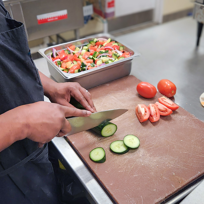 Culinary team member at The Boulevard Senior Living Wentzville chops fresh cucumbers and tomatoes.