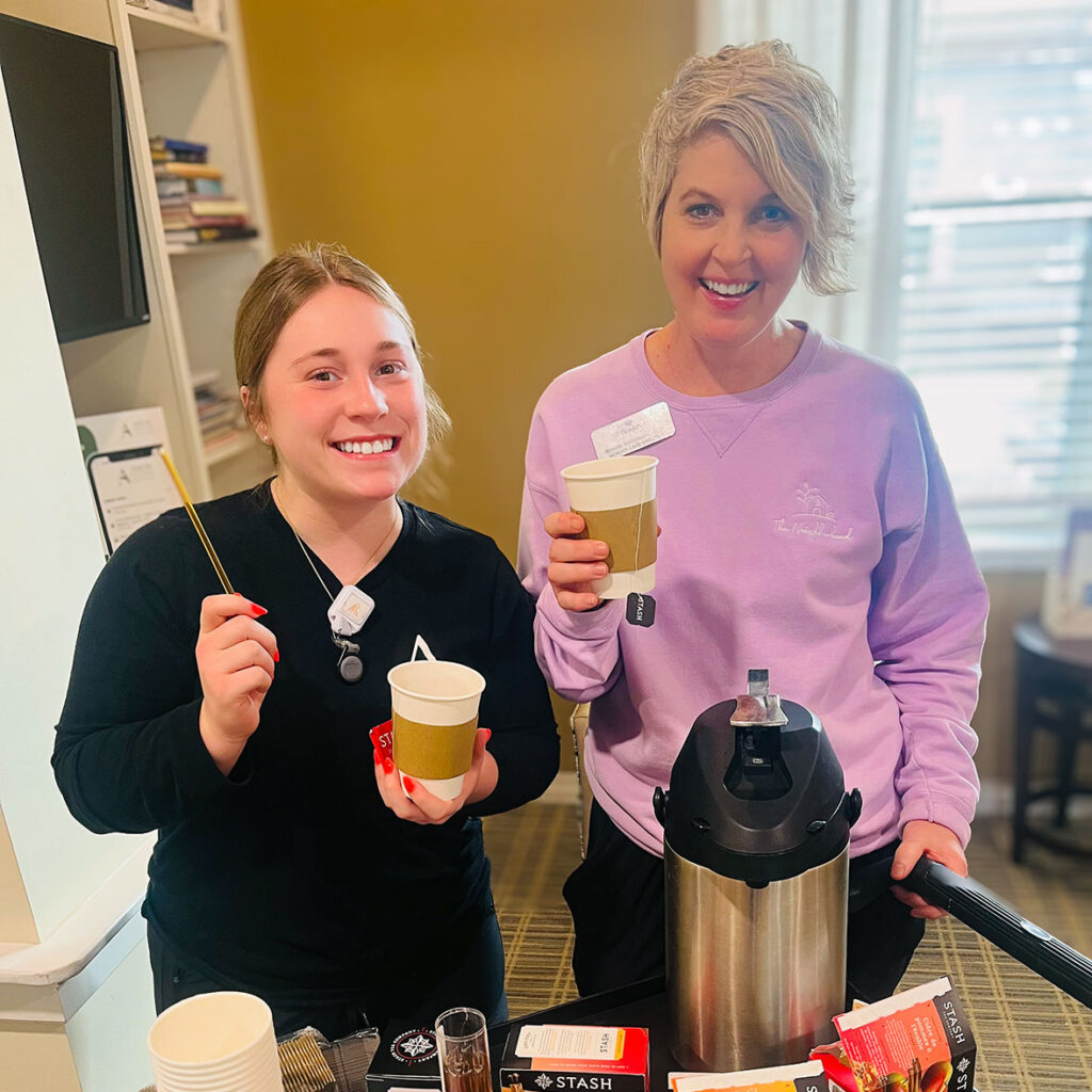 Two team members smile, holding cups of hot tea, during a team gathering.